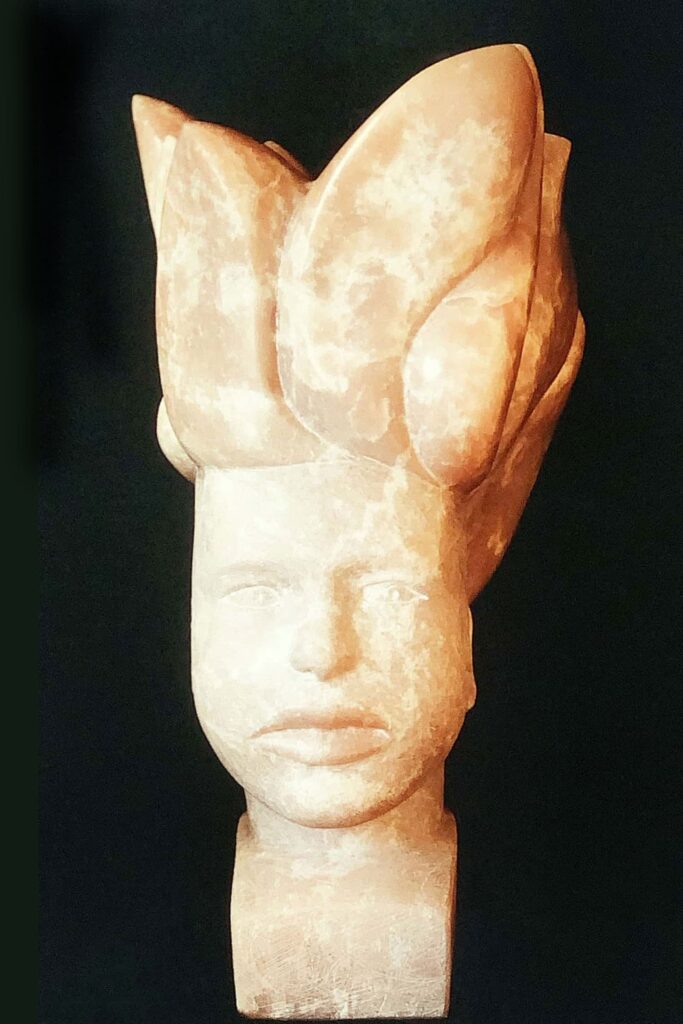 Skulptur eines Kopfes von vorne mit steiler Locke aus rosa Speckstein, die einen Berggott darstellt.